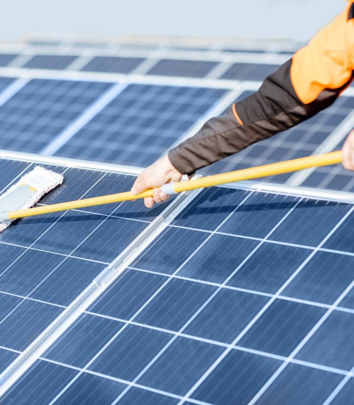 Professional cleaner in protective workwear cleaning solar panels with a mob. Concept of solar power plant cleaning service